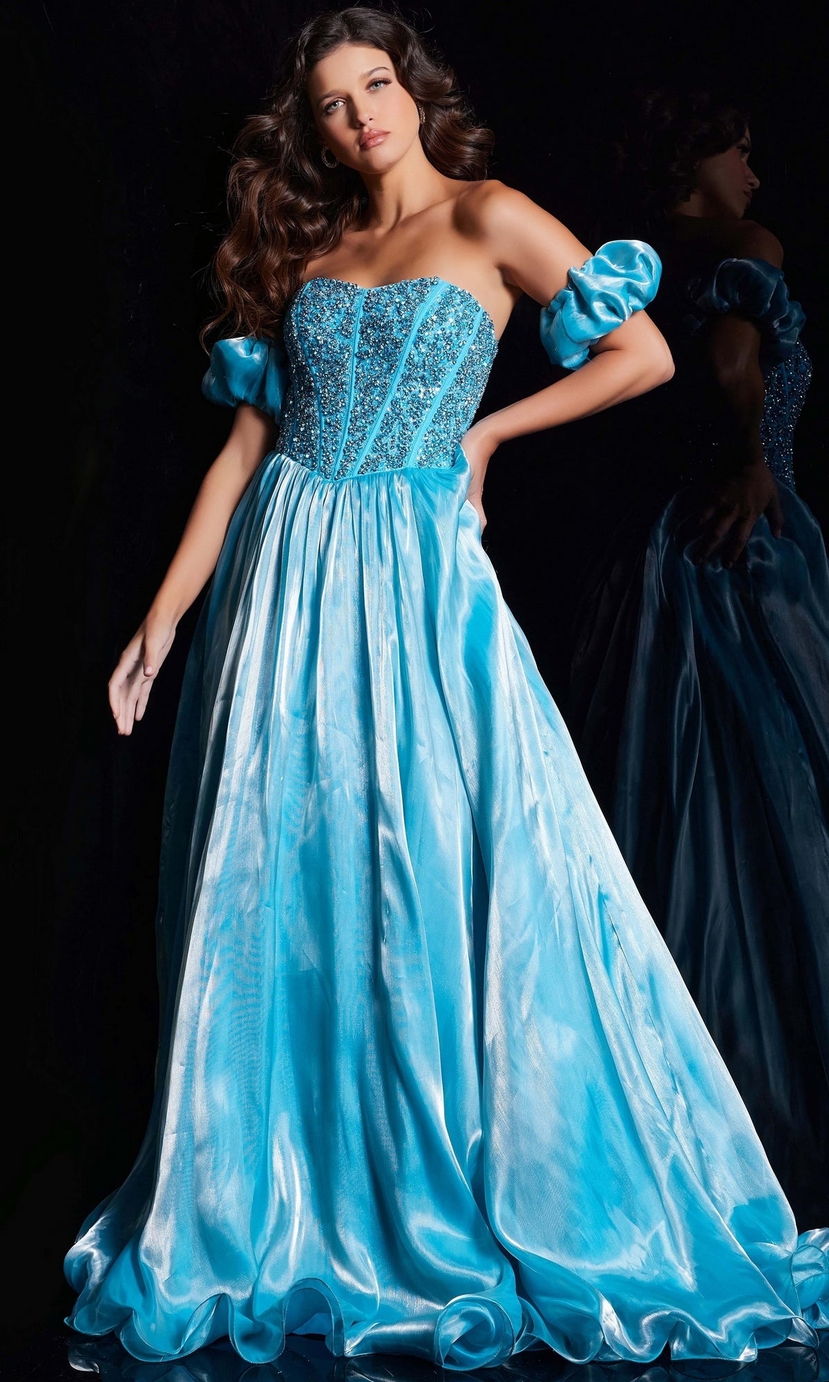 A woman models the Long Prom Dress 36591 by Jovani—a strapless, sparkling blue A-line ball gown with beaded corset and matching removable puff sleeves—posed against a dark background.